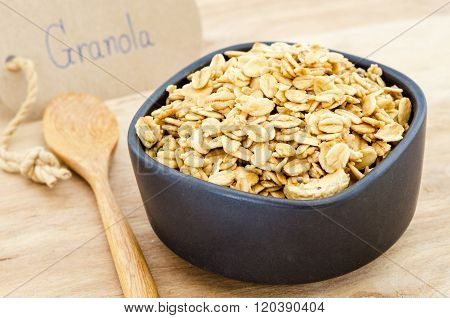 granola in bowl and wooden spoon on wooden background.