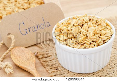 Homemade granola in white cup and wooden spoon with granola paper tag on sack background.