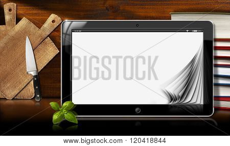 Tablet computer with blank pages and a stack of books in a kitchen with cutting boards and kitchen knife. Template for recipes or food menu