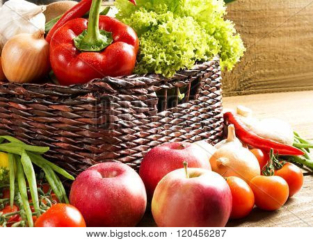 wicker basket with many fruits and vegetables on wooden table