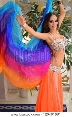 Beautiful brunette, belly dancer with rainbow shawl in the arabic harem interior