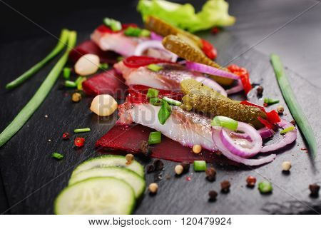 Herring Appetizer With Beets And Gherkin On Black Slate Board