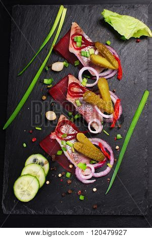 Herring Appetizer With Beets And Gherkin On Black Slate Board