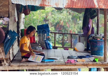 KO MOOK ISLAND, THAILAND, JANUARY 06, 2016 : A young girl is doing her homework, sitting outside on the home wooden terrace in Ko Mook island, Thailand