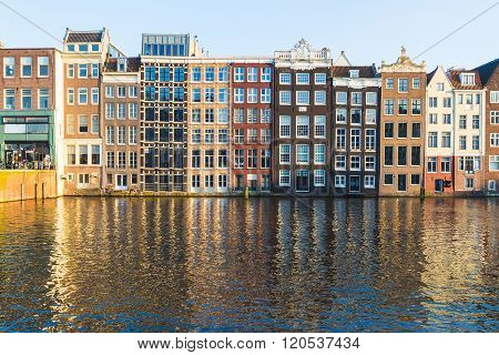 Old Buildings along the Damrak in Amsterdam during the day. Reflections can be seen in the water.