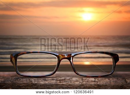  hipster glasses on a park bench or table with a beach in the background toned with a retro vintage instagram filter app or action effect 