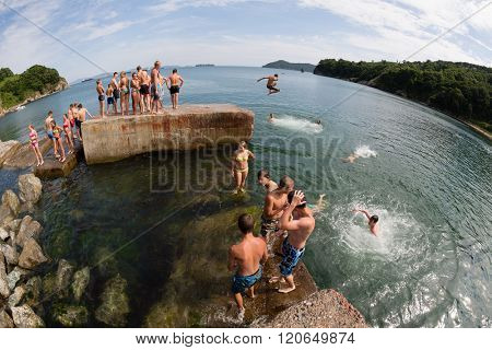NAKHODKA, RUSSIA - CIRCA AUGUST, 2015: Joyful children jumping and diving into the sea from the old dock. Local children love to relax, sunbathe, swim and dive in the sea bay near the Nakhodka city