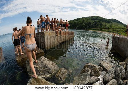 NAKHODKA, RUSSIA - JULY 29, 2015: Joyful boy and girl jumping into the sea from the old pier. Local children love to relax, sunbathe, swim and dive in the sea bay near the city of Nakhodka.