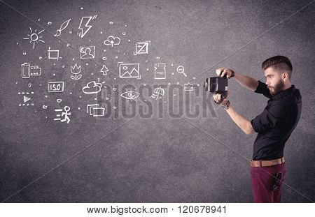 An elegant hipster guy trying to use a vintage camera with camera settings icons drawn on wall, like flash, white balace or ISO value concept