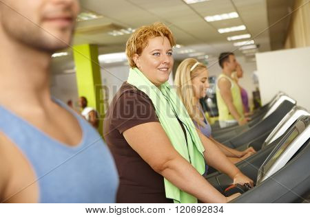 Fat woman training in gym, using running machine.