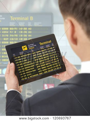 Businessman with tablet in airport with flight schedule and departure and gate information
