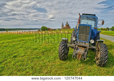 KIZHI ISLAND, RUSSIA - AUGUST 2015: Old rusty tractor on a field with monastery in background 