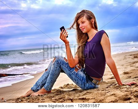 Girl with mobile phone sitting on sand near sea and blue sky. First love.