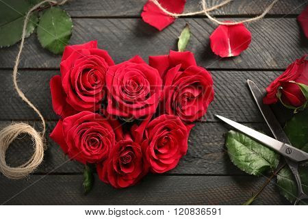 Fresh red roses buds in shape of heart with rope and scissors on wooden background