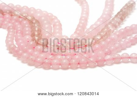 Strings of pink quartz for making jewellery on white background