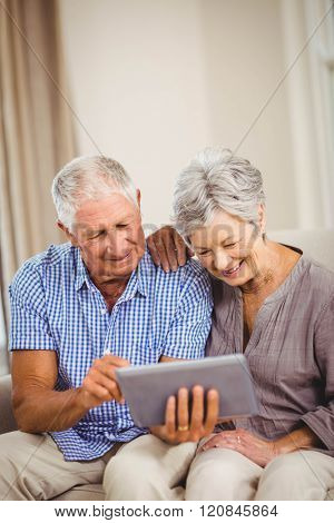 Senior couple sitting on sofa and looking at digital tablet in living room