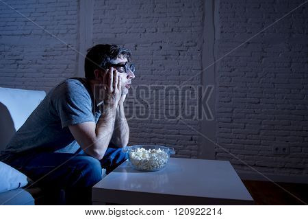 young television addict man sitting on home sofa watching TV and eating popcorn wearing funny nerd and geek glasses looking mesmerized enjoying movie sitcom or live sport at night