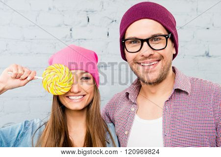 Portrait Of Happy Young Comic Couple In Hats Holding Lollipop