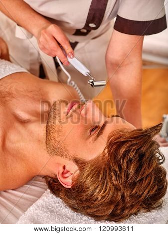 Man enjoying electric galvanic face and neck spa massage at beauty salon. 