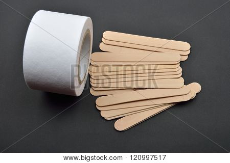 Picture Of Many Wooden Spatulas And Roll Of Paper For Wax Depilation On Black Background