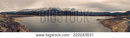 Panoramic view of Lac de Codole and dam wall in the Balagne region of Corsica with snow covered mountains in the distance