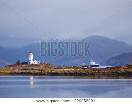 Lighthouse on Isle of Ornsay, the southern side of Isle of Skye, Scotland. Trade ship at rocky island, mountains in background
