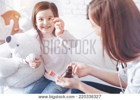 Take medicine with pleasure. Positive delighted female child keeping smile on her face and embracing white bear while expressing positivity