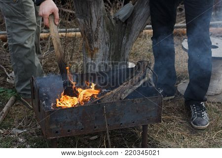 Two young men ignite the wood in the grill, going to fry a shish kebab.