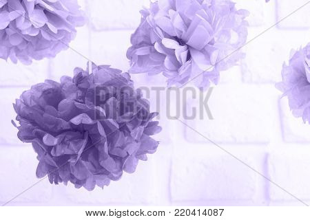 Paper flowers at the baby shower party.  Party decoration and celebration concept. Festive party background. Horizontal, white brick background. Ultra violet tone, color of the year 2018