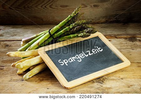 Green and white asparagus and a  blackboard with the word german Spargelzeit, that means asparagus time, on a rustic wooden background, selective focus, narrow depth of field