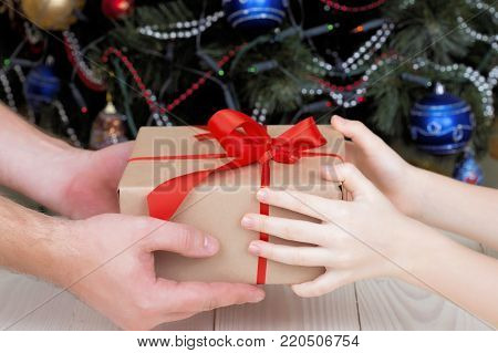 Crop father gives a Christmas gift to the child. A gift with a red ribbon from hand to hand. A surprise at Christmas.