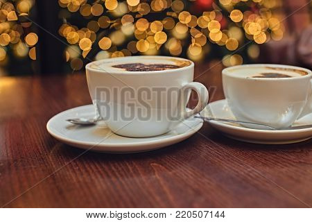 Two white cups with aroma refreshing coffee on a table with illumination lights on the background.