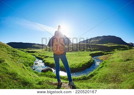woman traveler with small orange backpack on a walk in the Valley of the river of Hveragerdi Iceland. Hiking Tour of Reykjadalur Hot Springs