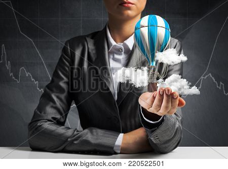 Closeup of business woman in suit presenting flying aerostate among clouds in her palm with business sketches on background. 3D rendering.