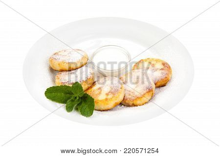cheese pancakes sprinkled with powdered sugaron on a white plate with sour cream, decorated with mint leaves on a white background
