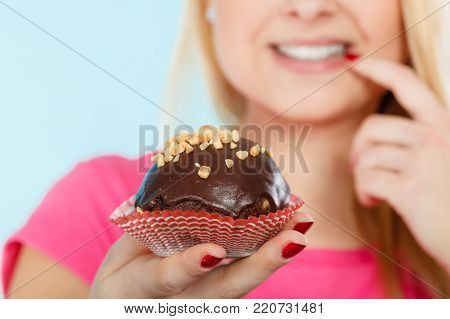 Diet, sweets, food concept. Woman holding delicious chocolate cupcake with peanut frosting about to take bite