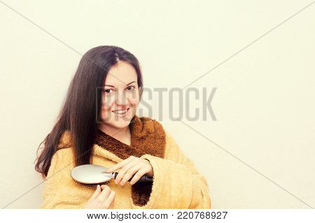 beautiful brunette girl combing her hair in a bathrobe