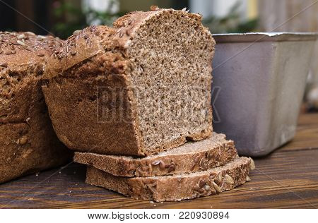 Half of homemade black bread with some bread slices and bread pan on background