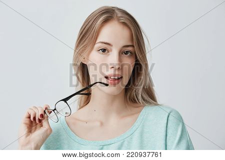 Horizontal shot of beautiful fair-haired thoughtful woman looks pensively aside with spectacles, being deep in thoughts, analyzes something in her mind, pensively looks at camera.