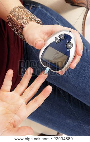 A young woman sitting in jeans testing her bloodsugerlevel with a
instrument