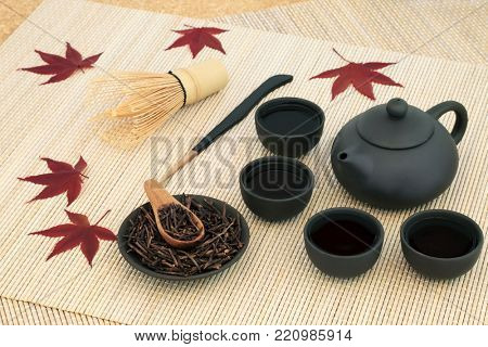 Japanese kuchika roasted twig green tea with teapot and cups, stirrer, whisk and maple leaves on bamboo background. Has many health benefits including rejuvenating properties.