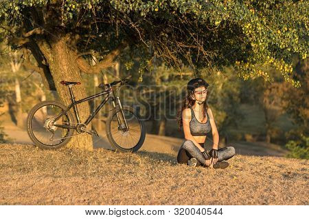 Girl On A Mountain Bike On Offroad, Beautiful Portrait Of A Cyclist At Sunset, Fitness Girl Rides A 