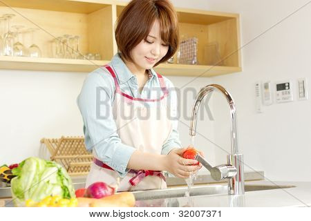 Smuk ung kvinde i køkken at lave salat. Portræt af asiatisk kvinde.