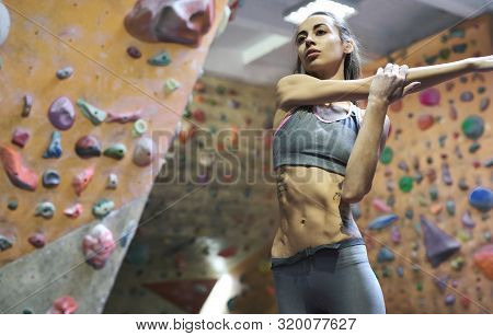 Athletic Woman With Muscular Naked Torso Doing Stretching Before Climb In Indoor Climbing Gym.
