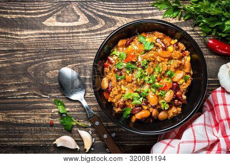 Chili Con Carne With Meat, Beans And Vegetables With Herbs On Wooden Table. Traditional Mexican Food