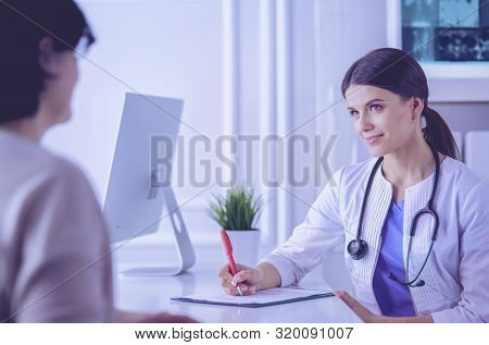 Doctor and patient discussing medical problems in a hospital consulting room. Doc filling in a patient's form