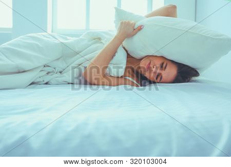 Young caucasian woman covering her head and ears with pillows.