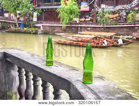 Two Green Beer Bottles On A Wooden Railing With A Blurred Background Of The Tuo Jiang River Within F