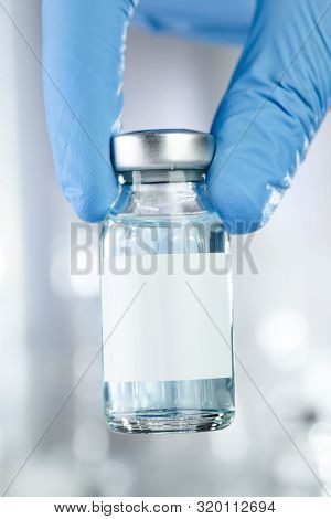 Healthcare concept with a hand in blue medical gloves holding a vaccine vial with blue liquid and black white label