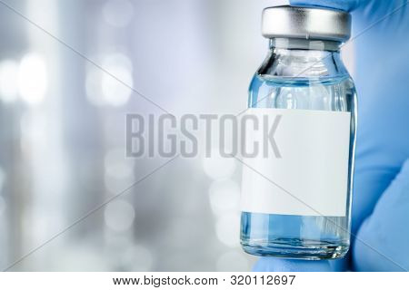 Healthcare concept with a hand in blue medical gloves holding a vaccine vial with blue liquid and black white label